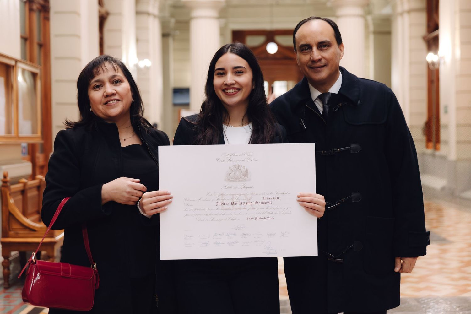 Family of three proudly displays graduation diploma in grand building corridor.