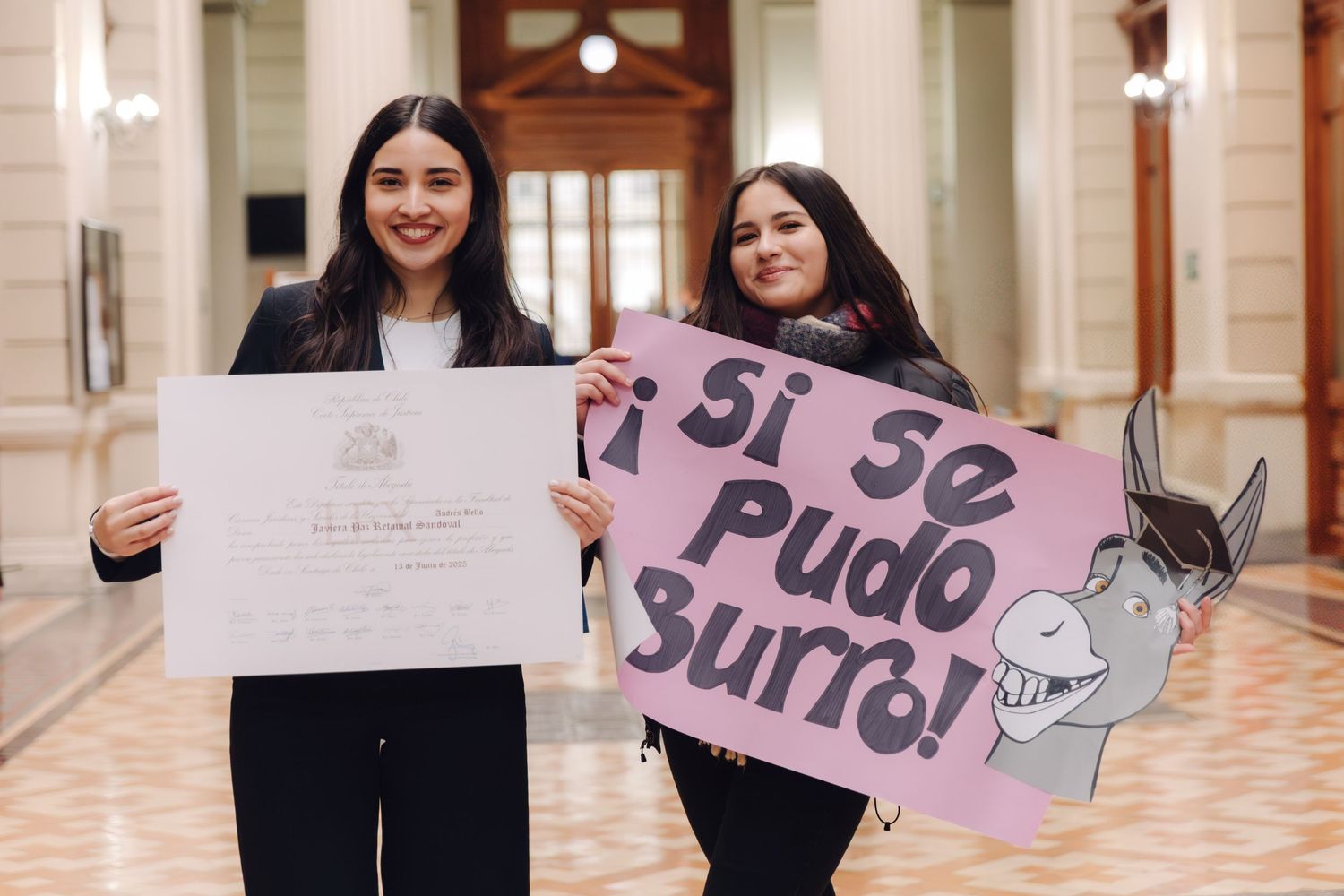 Two young women celebrate graduation with diploma and congratulatory sign.
