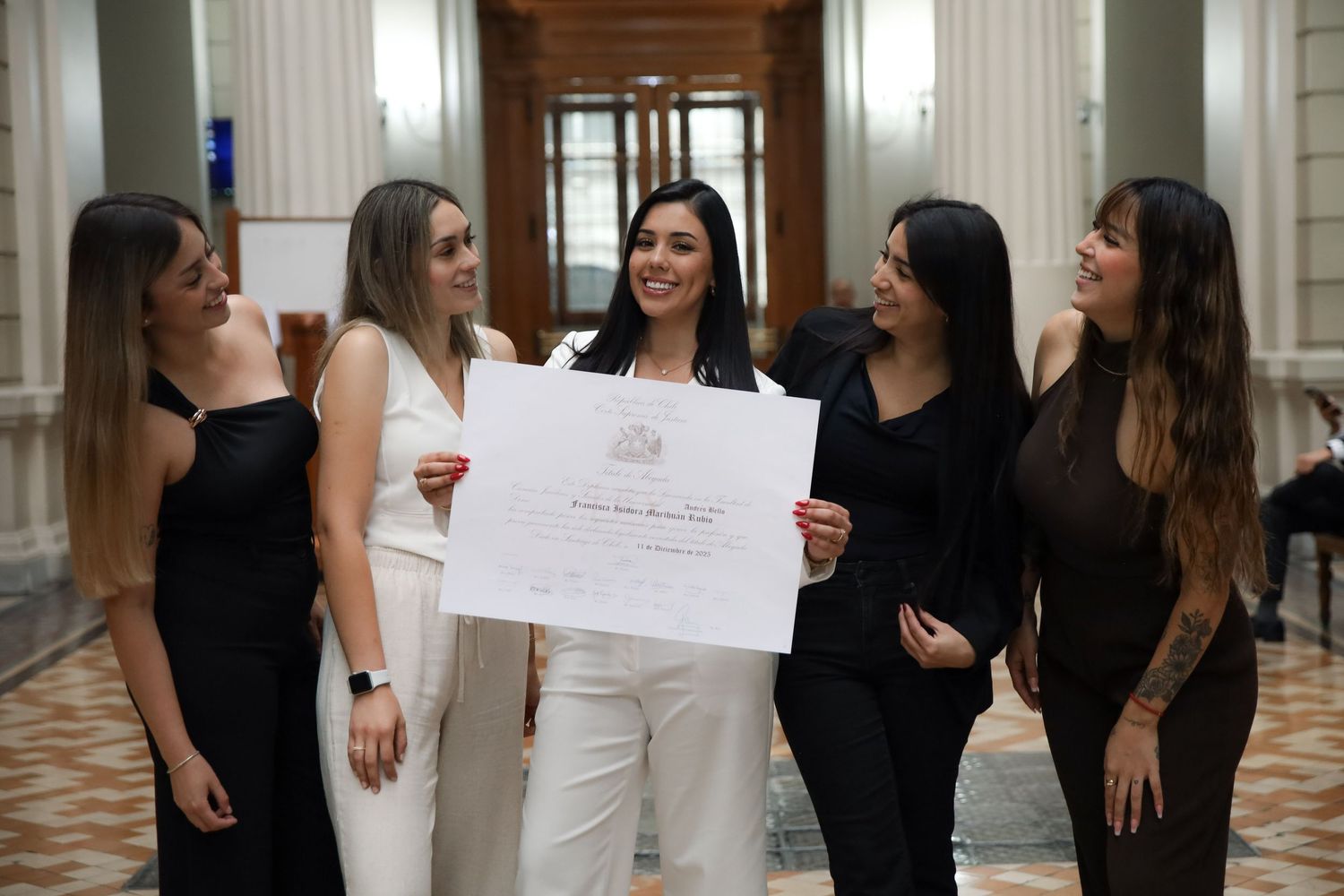 Graduate in white suit celebrates with four friends holding diploma in classical interior hall.