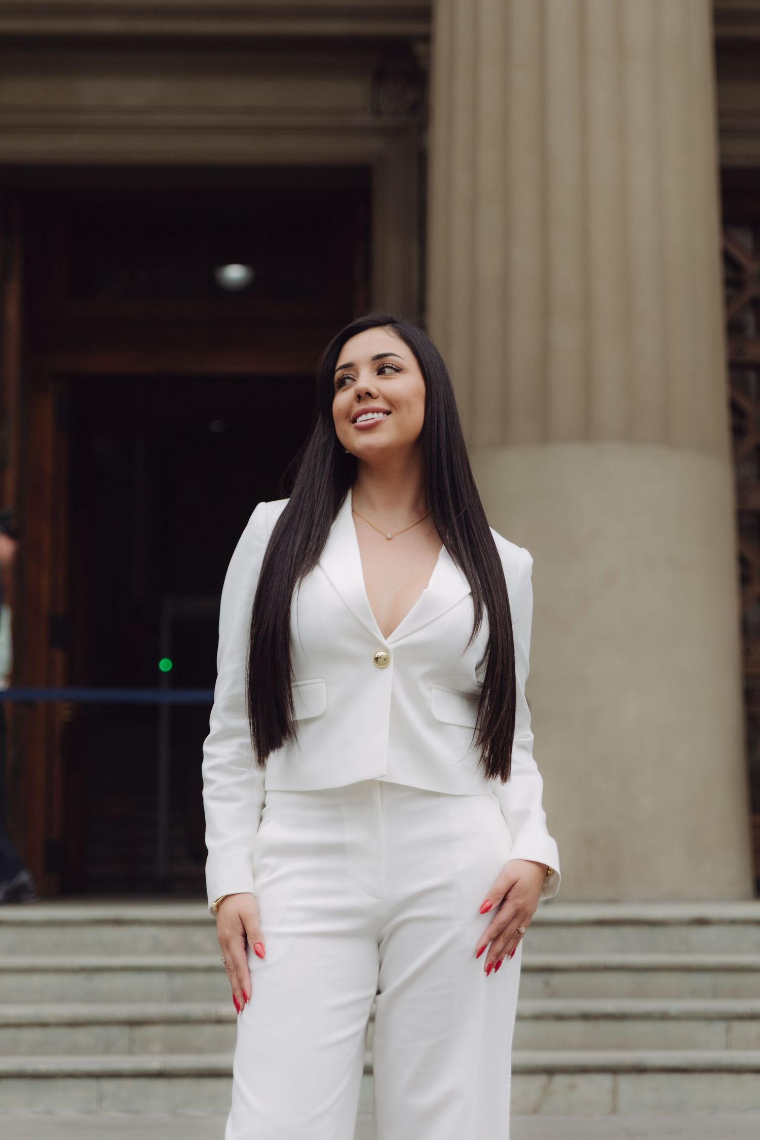 Smiling woman in white suit standing on steps of neoclassical building with columns.