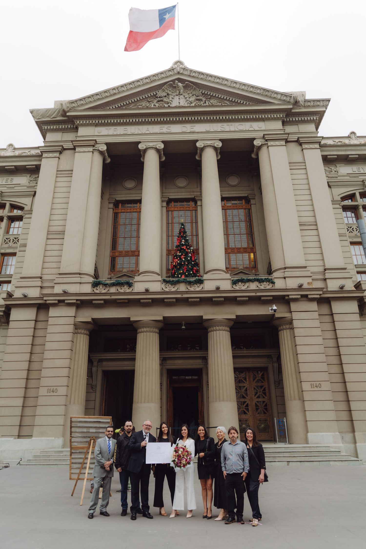 Group of people holding diploma outside neoclassical building with Chilean flag above.