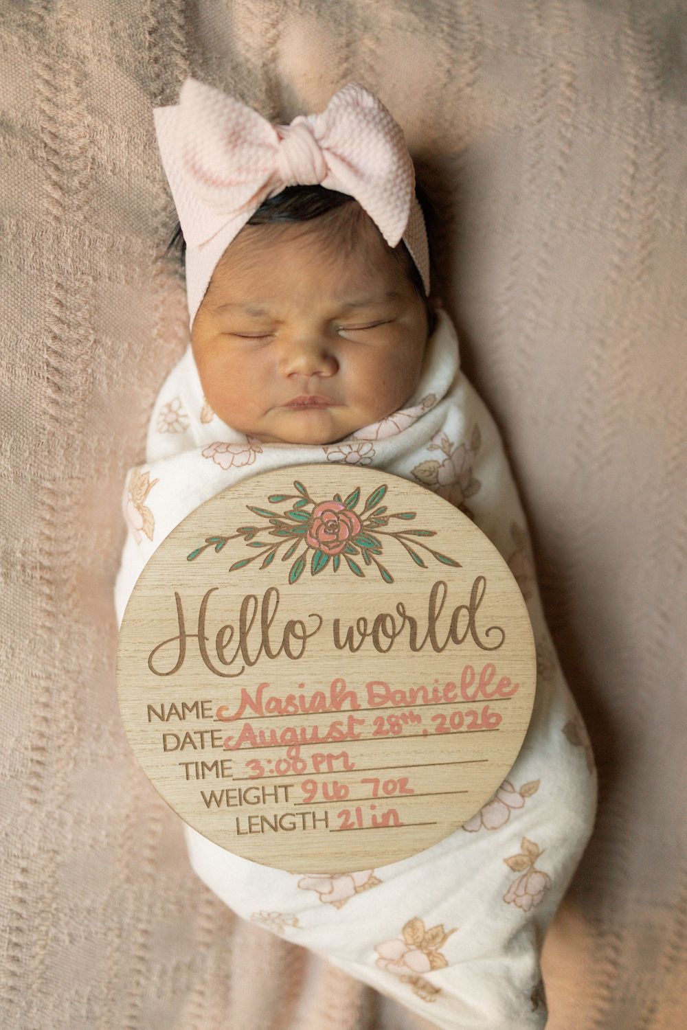 Newborn baby girl Nasiah Danielle swaddled in floral wrap with pink bow, birth announcement sign, born August 29 2026.