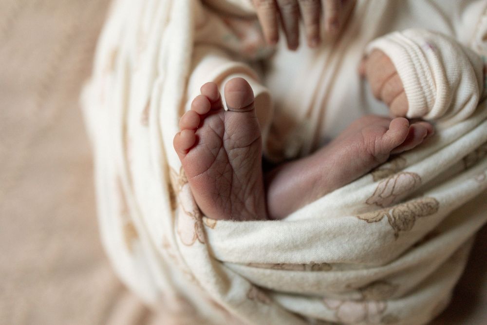 Close-up of newborn baby feet wrapped in a soft cream swaddle blanket, perfect for birth announcements.
