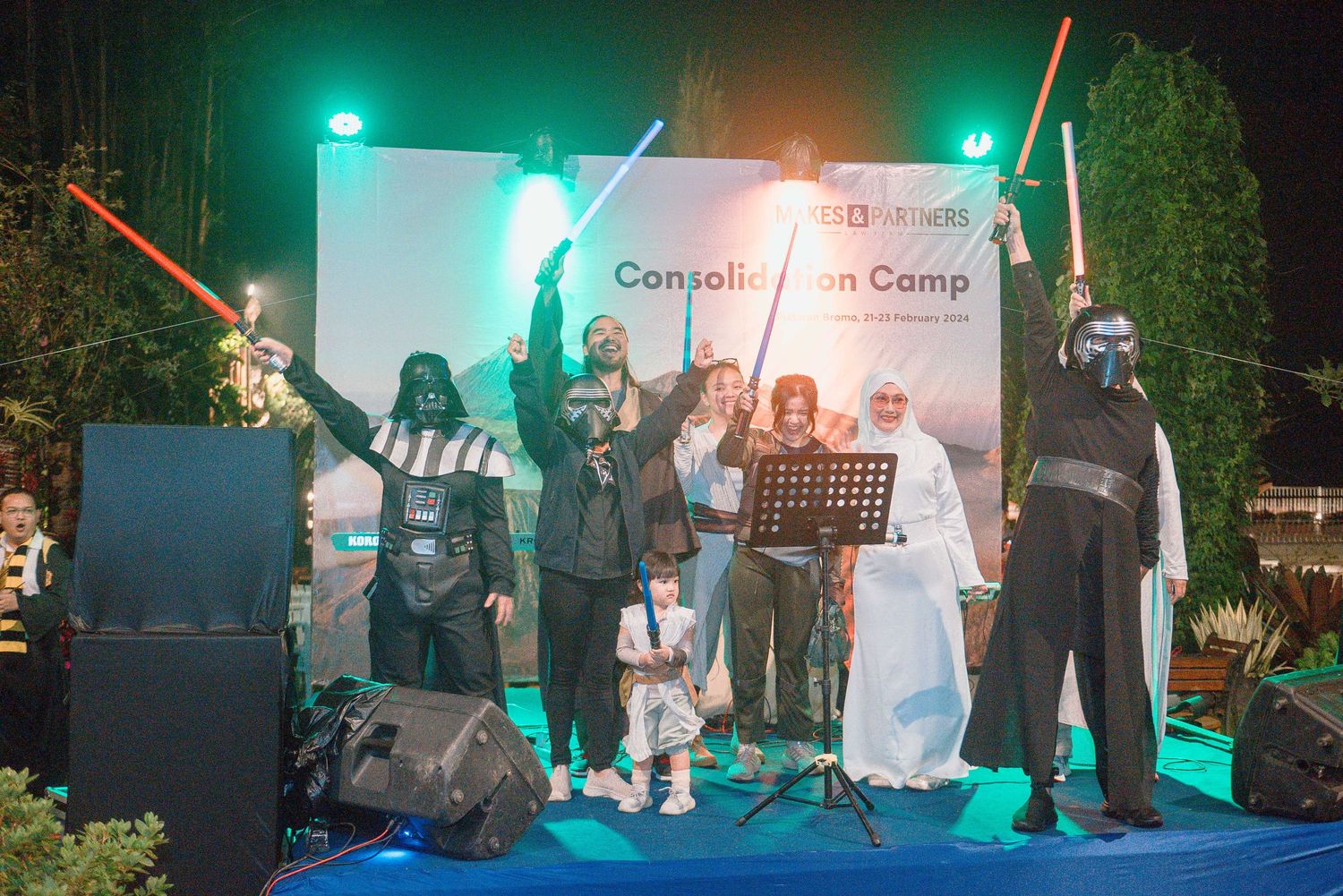 Star Wars costumed characters pose with guests at a Consolidation Camp event on an outdoor stage at night.
