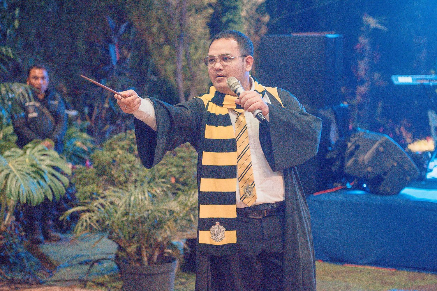 Man in Hufflepuff Harry Potter costume holds wand at cosplay event.