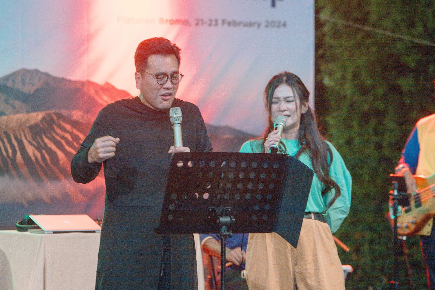 Two performers singing on stage at an outdoor event on February 21-23, 2024, with a mountain backdrop.