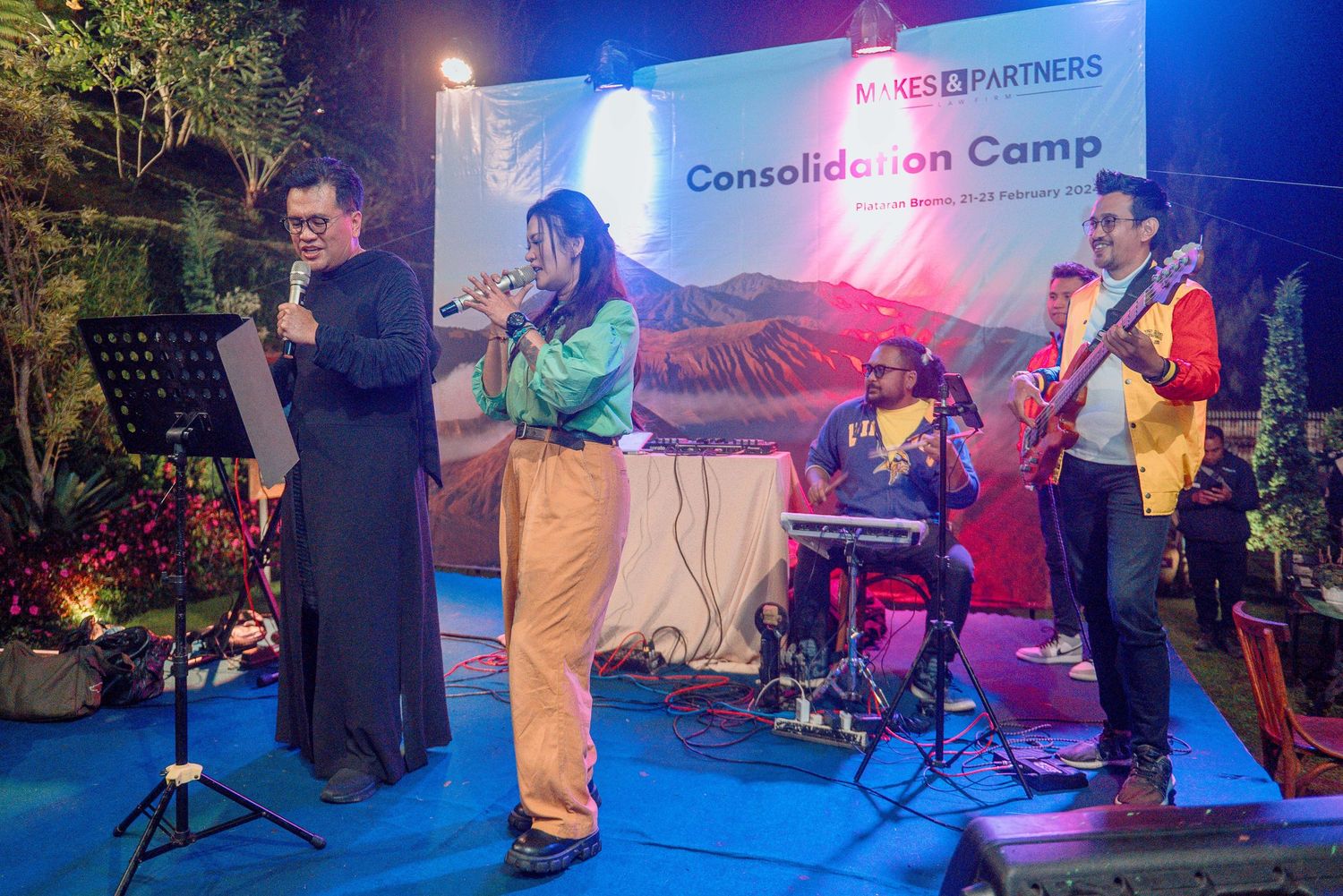 Live band performing at Makes & Partners Consolidation Camp corporate event on an outdoor stage at night.