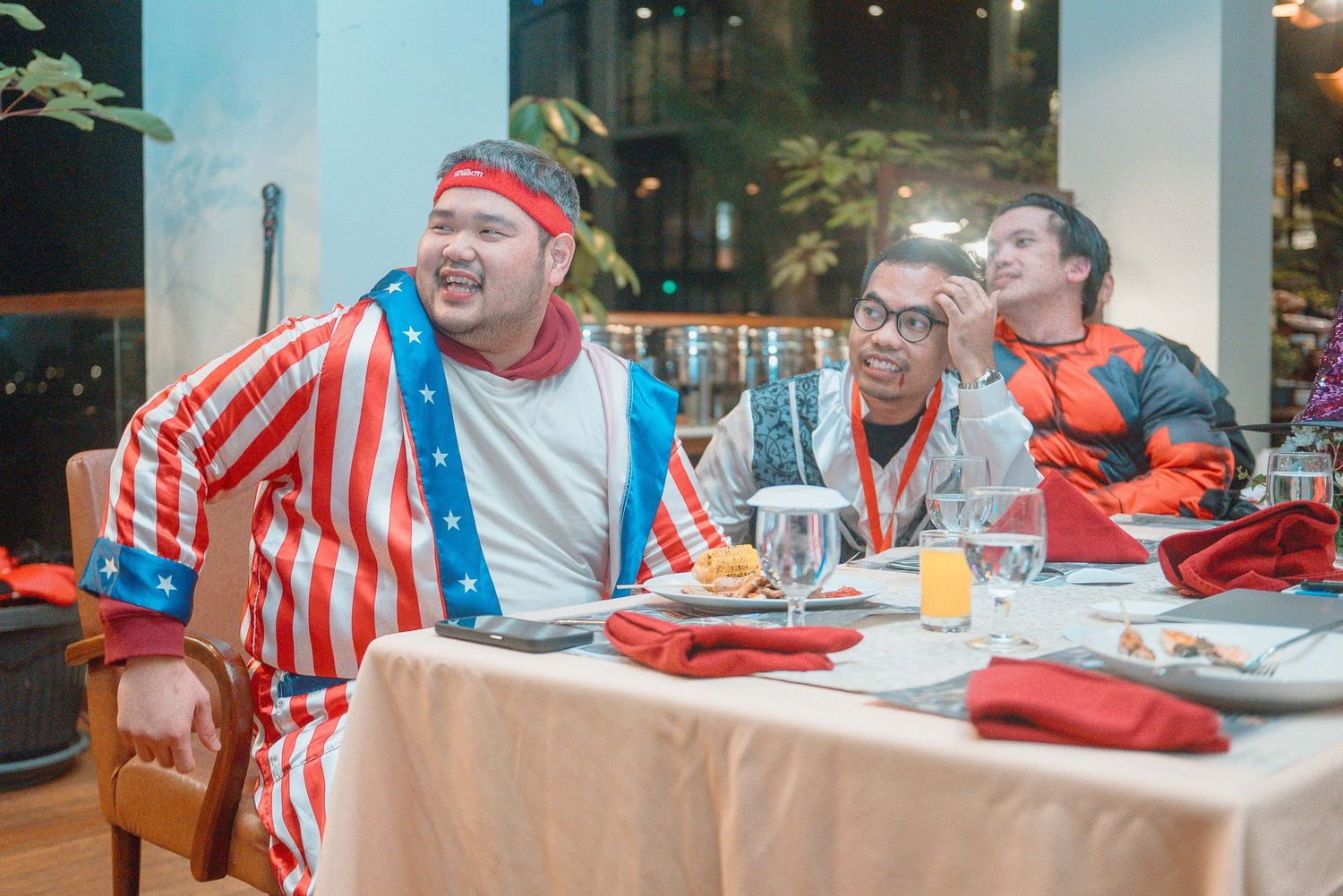 Three men in patriotic costumes dining at a festive table with American flag decorations and drinks.