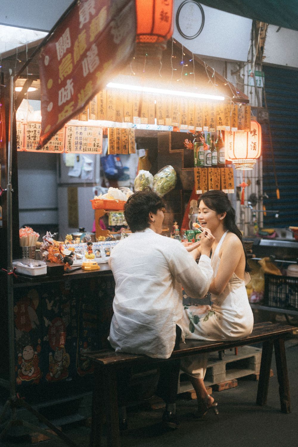 Couple sharing a romantic meal at a glowing Asian street food stall at night.