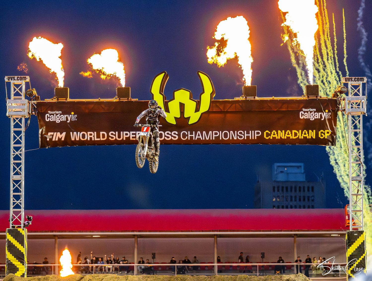 Motocross rider soars over a jump at the FIM World Supercross Championship Canadian GP with dramatic fire pyrotechnics.