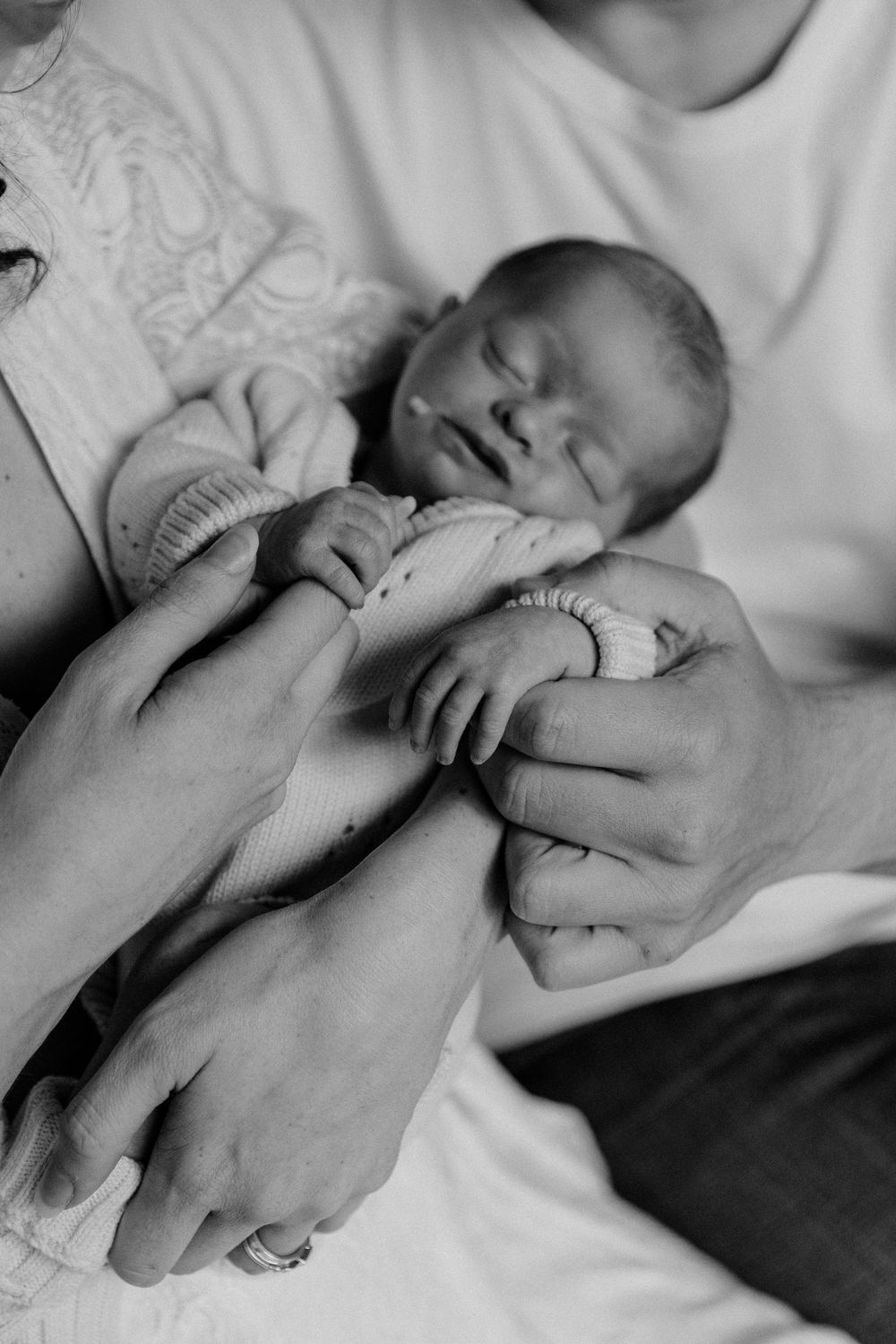 Black and white photo of newborn baby sleeping peacefully in parents' loving hands.