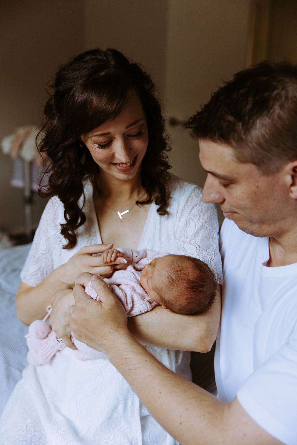 Happy parents smiling at their newborn baby wrapped in pink, sharing a tender family moment together.