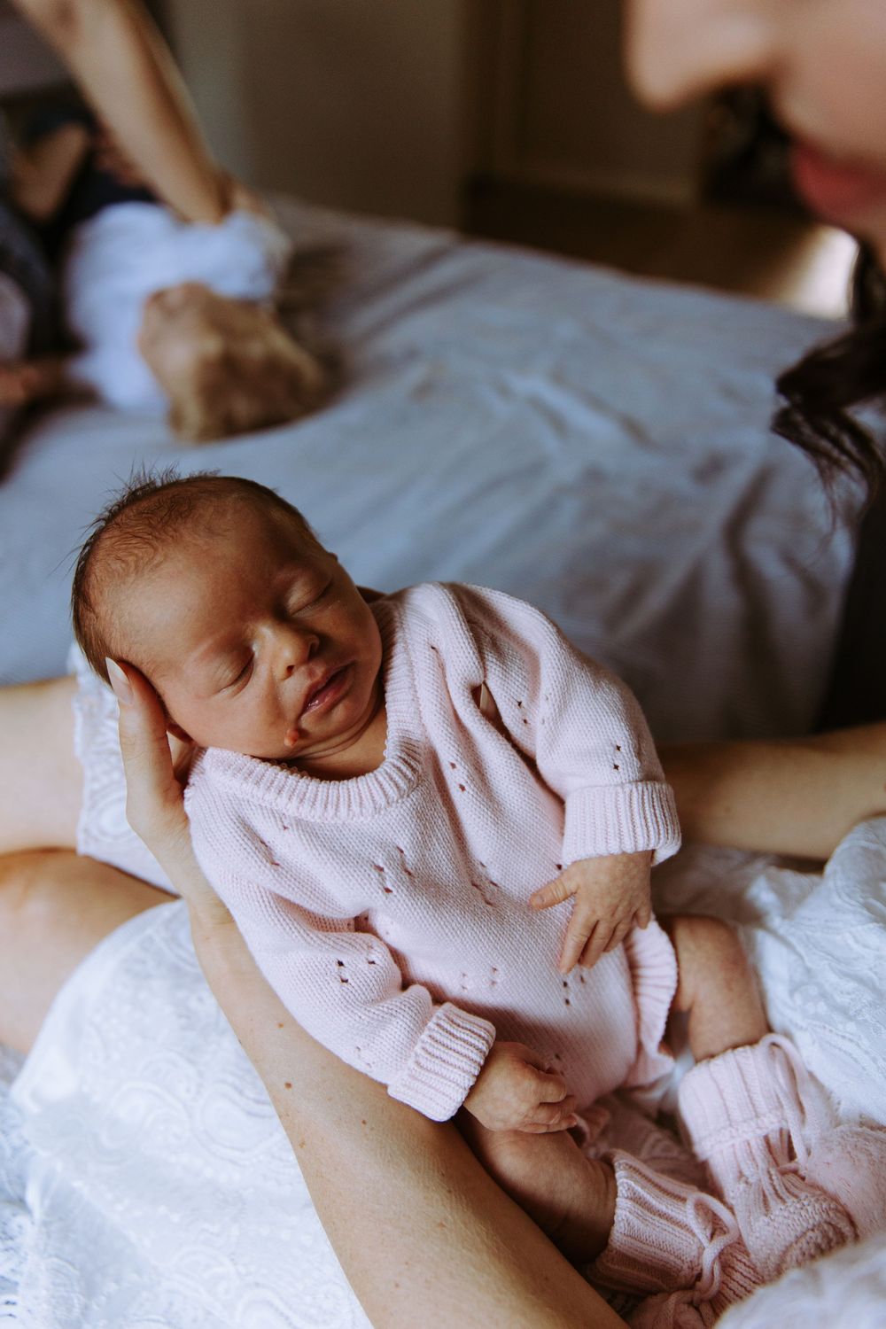 Newborn baby in pink knit outfit sleeping peacefully in mother's arms during a lifestyle newborn photography session.