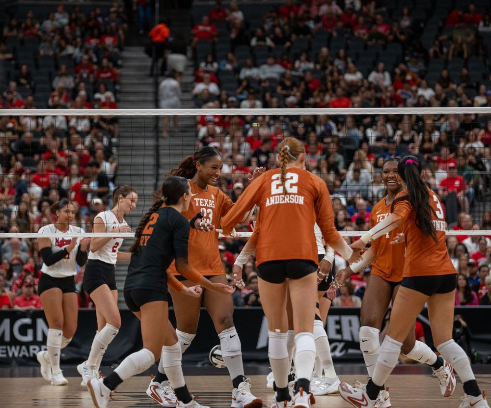 Texas Longhorns volleyball team celebrating a point during a competitive match in an arena.