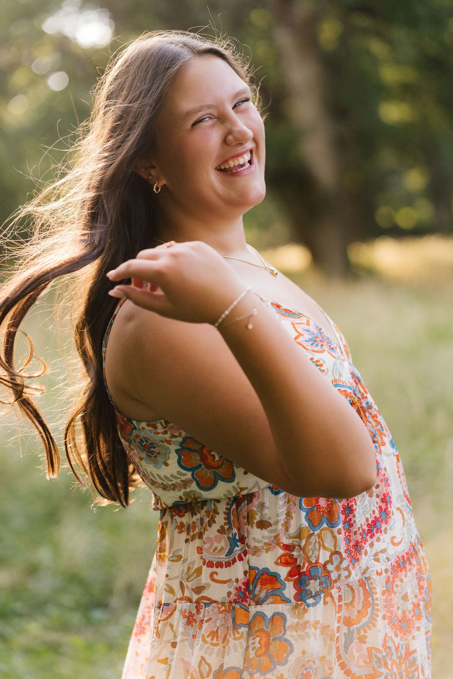 Young woman smiling in a floral paisley sundress outdoors in a green field.