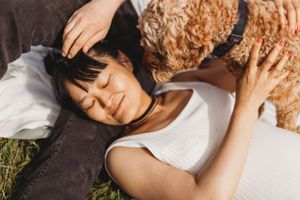 Person lying on grass cuddling with curly-haired dog in sunlight.