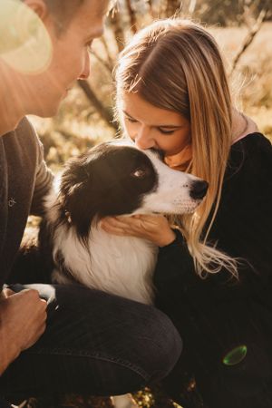 A couple snuggles with their Border Collie dog during a golden hour photoshoot.