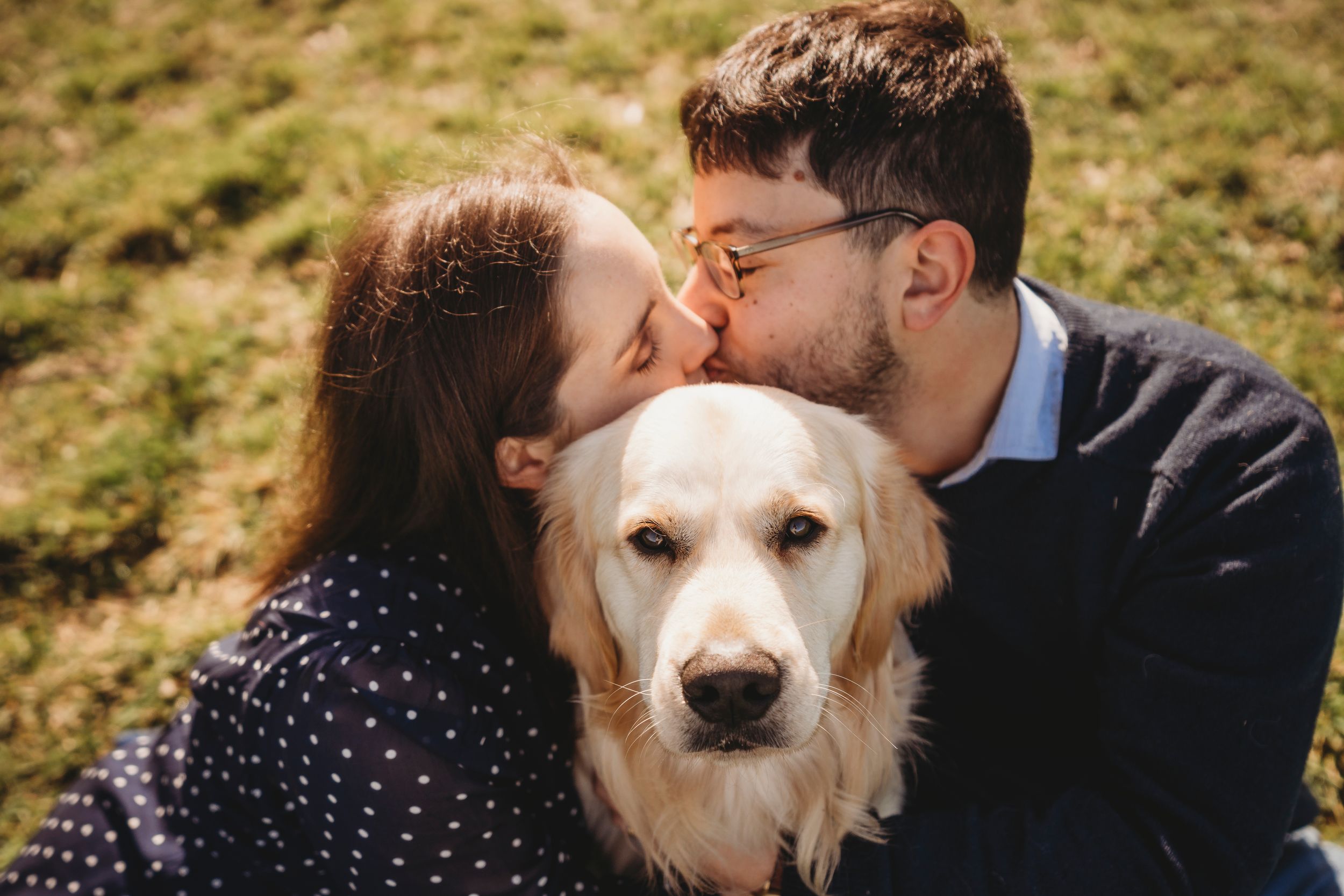 Couple sharing affectionate moment with their golden retriever between them outdoors.