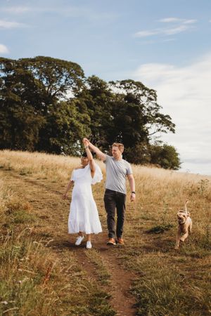 A couple dances along a hilltop trail with their dog following behind in golden sunlight.