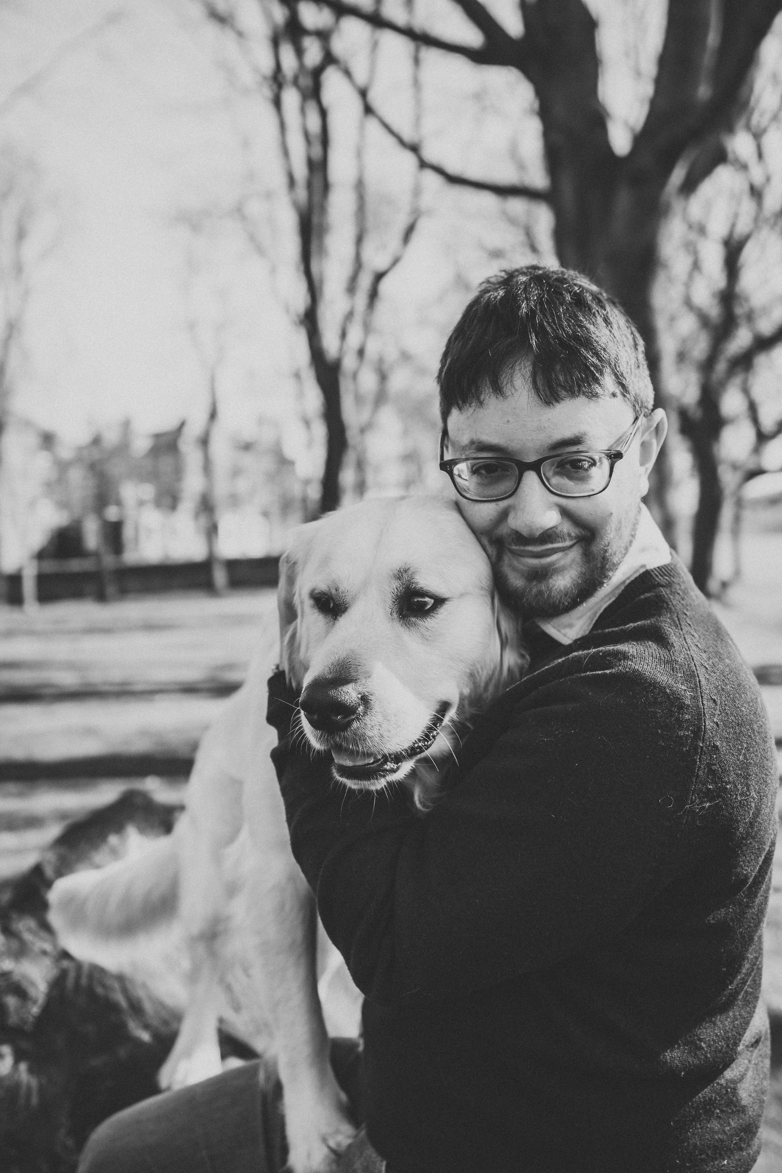 Smiling individual embracing golden retriever outdoors in black and white photography.