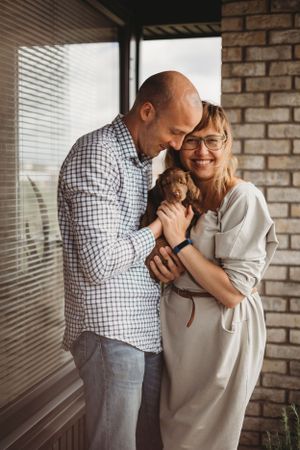 A couple shares a tender moment while holding a small brown puppy against a brick wall background.