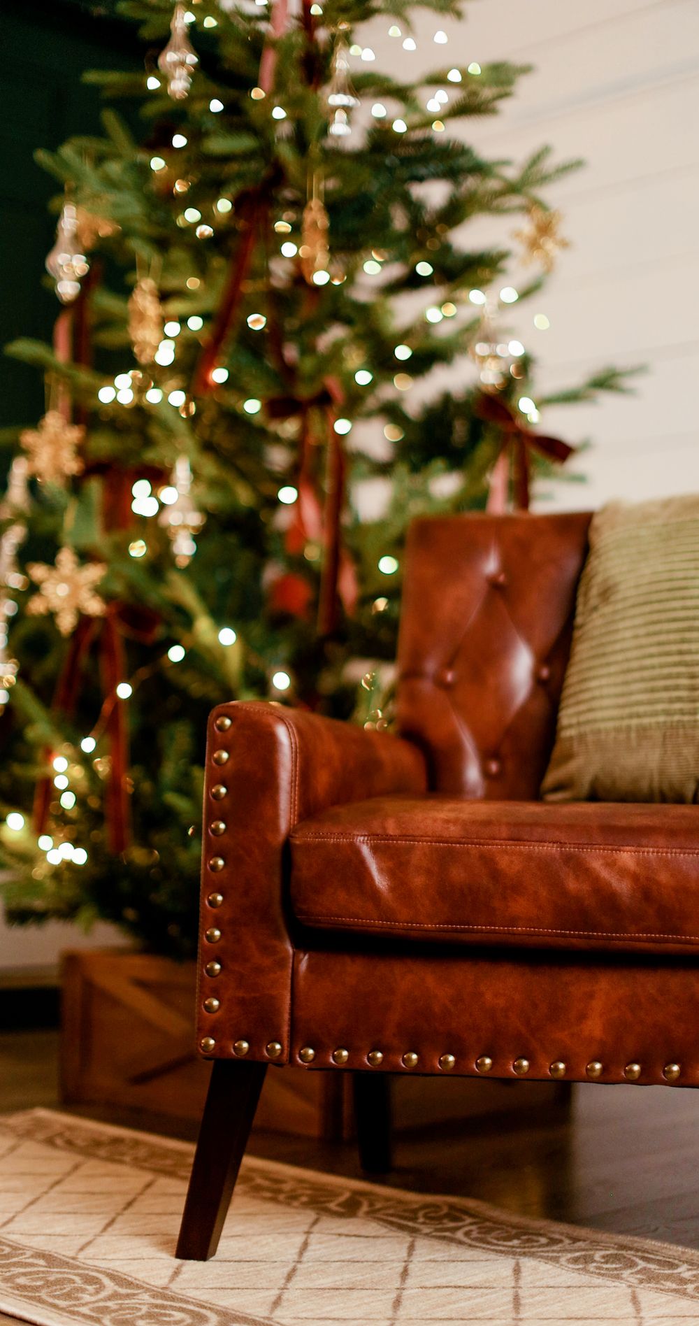 Brown leather tufted armchair with brass nail head trim beside a decorated Christmas tree with warm fairy lights.