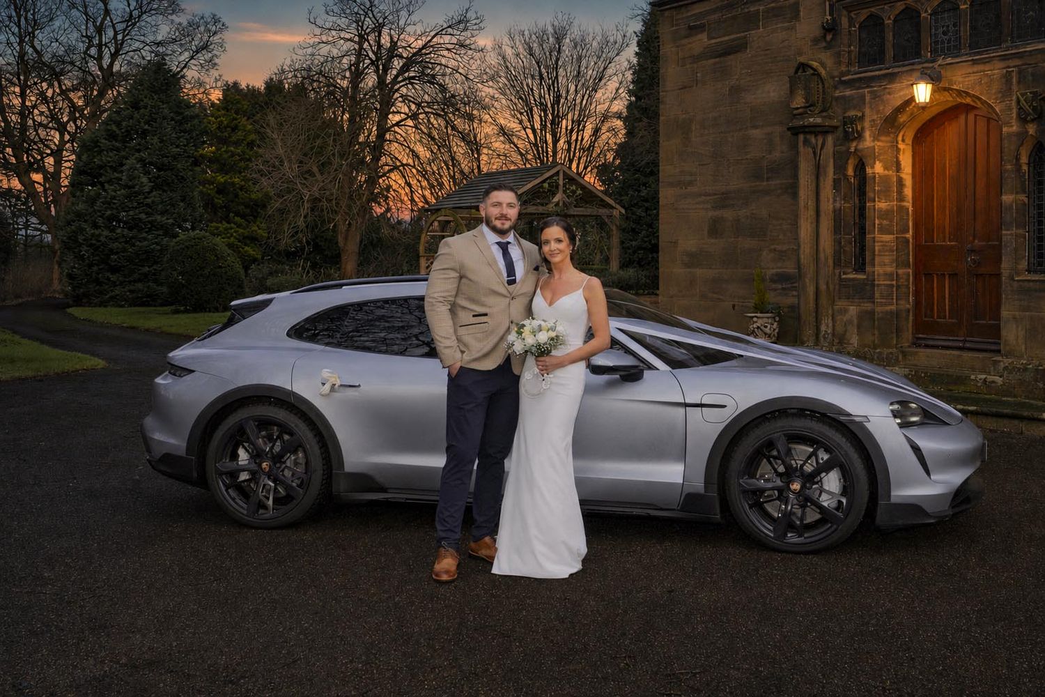 Bride and groom posing beside a silver Porsche outside Lady Gillford's House Registry Office in Carlisle