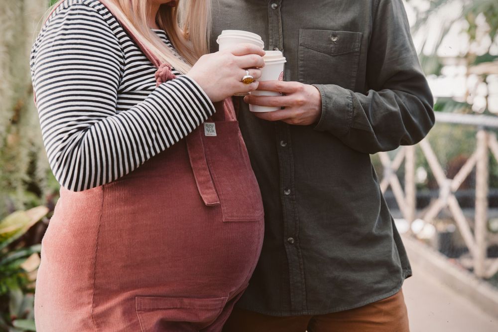 close up of couple cheersing coffee cups showing pregnant belly
