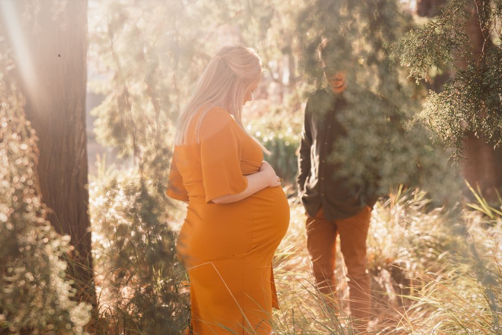 Couple pregnant walking in trees at the gardens in Christchurch with golden light