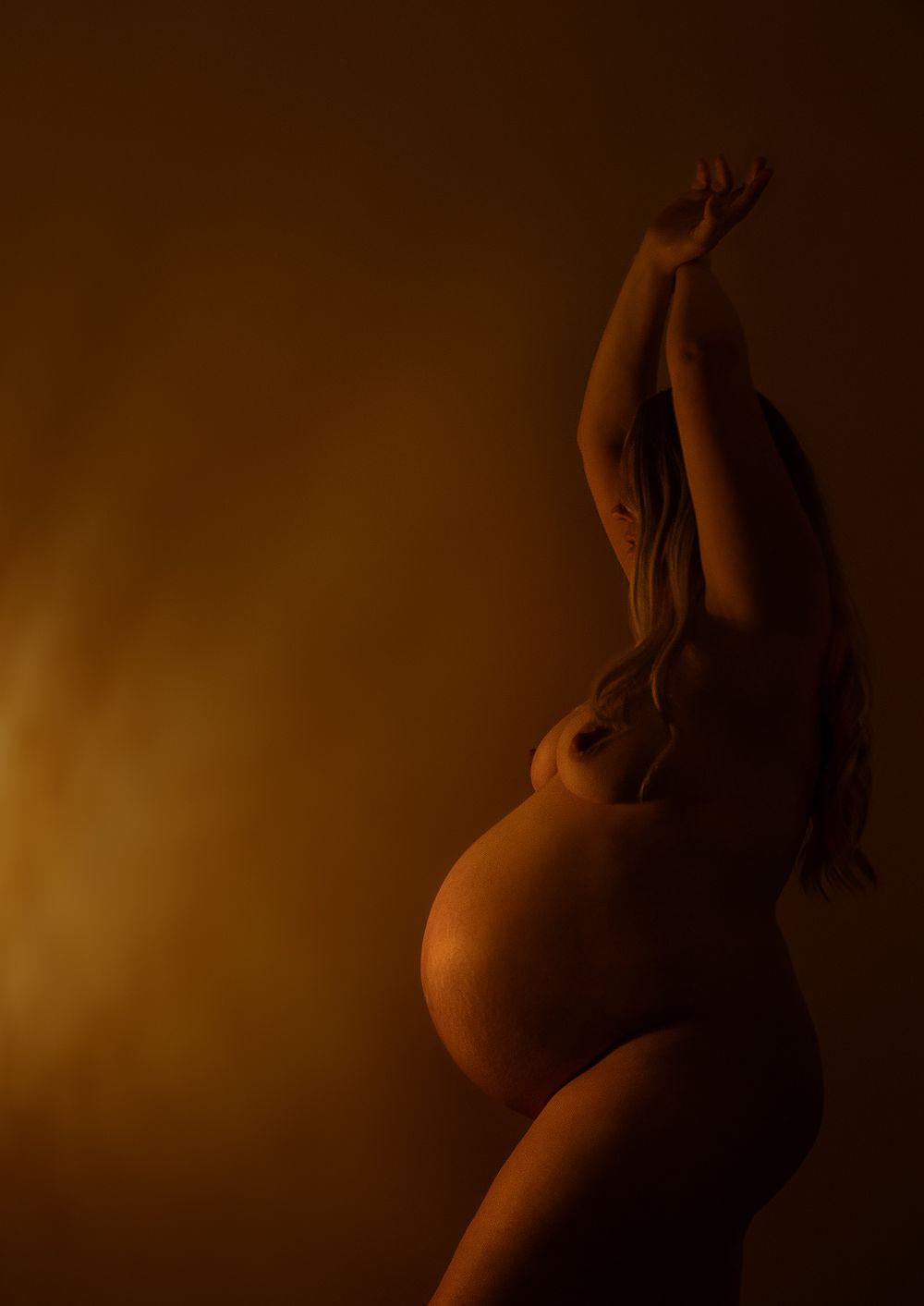 Side profile of a naked pregnant lady in soft glowing light
