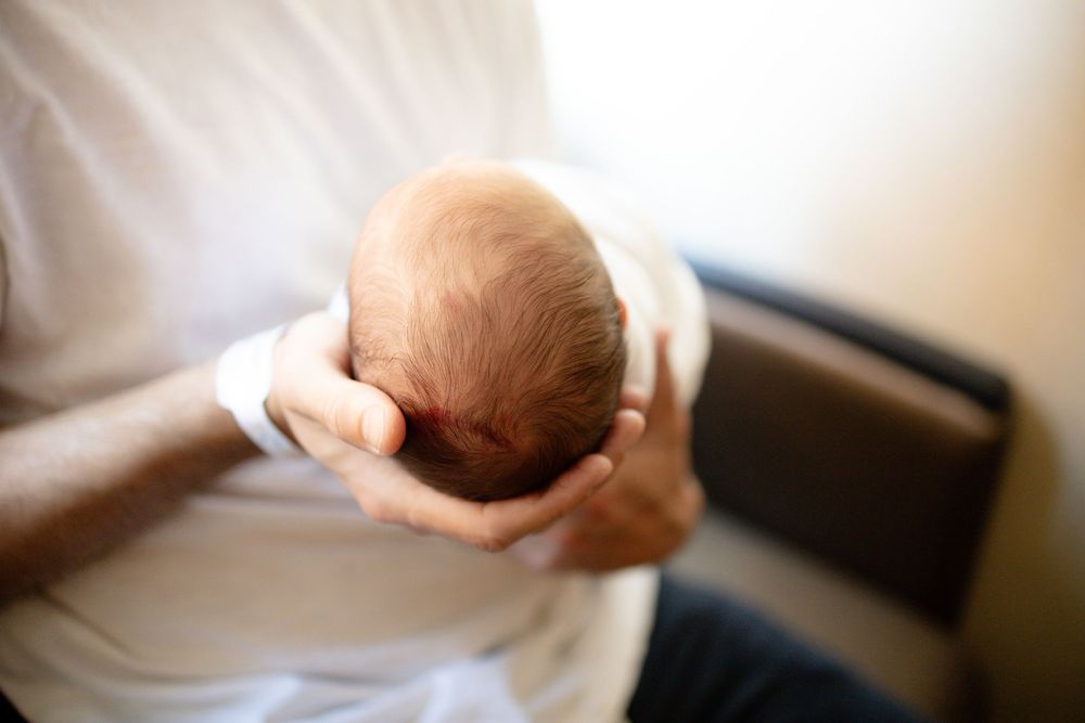 Close-up of a parent gently cradling a newborn baby's head in their hands while seated indoors University of Tennessee Medical Center.