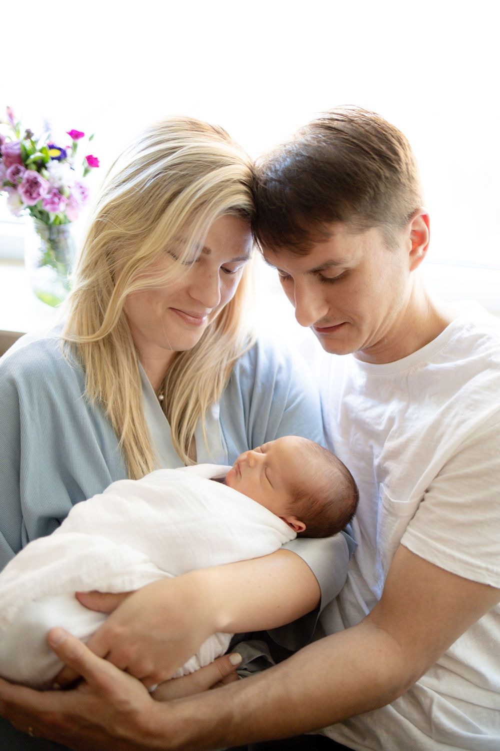 Young couple tenderly holding their newborn baby wrapped in white, smiling lovingly in a bright room University of Tennessee Medical Center.