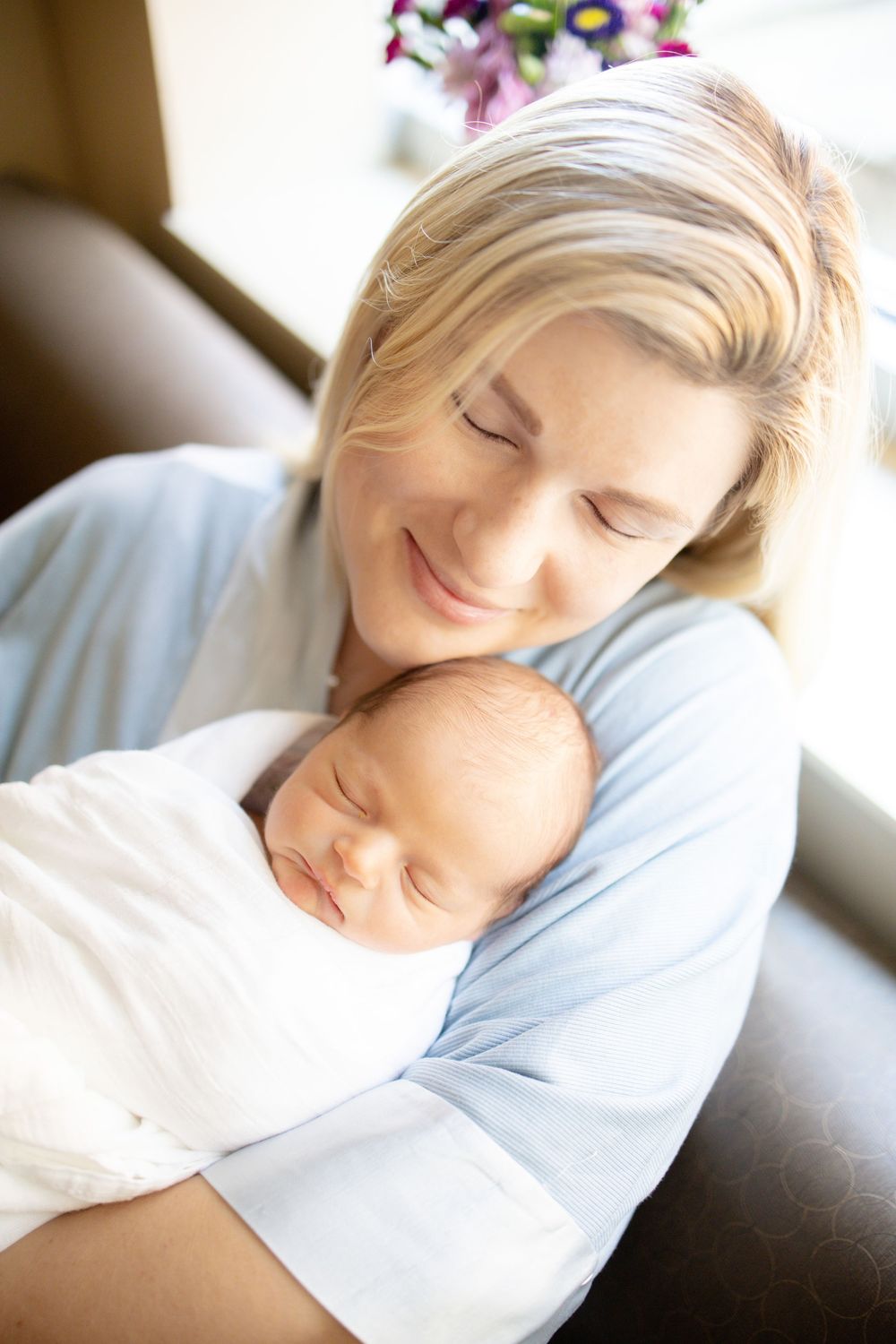 Smiling blonde mother tenderly holding her sleeping newborn baby wrapped in a white blanket University of Tennessee Medical Center.