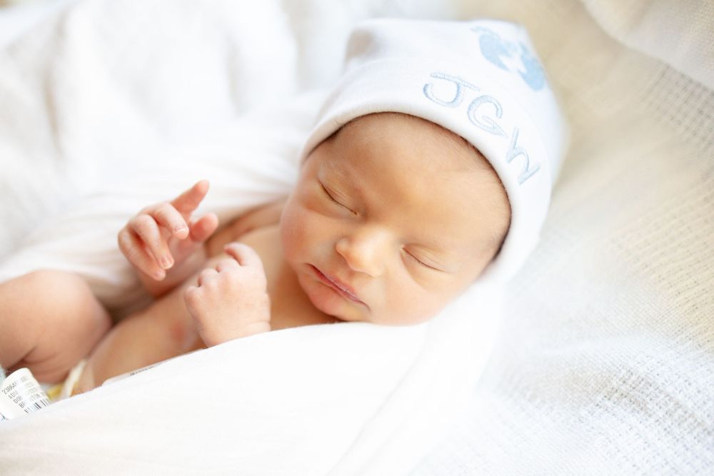 Peaceful newborn baby sleeping in white swaddle blanket wearing a white hat with blue accents in hospital University of Tennessee Medical