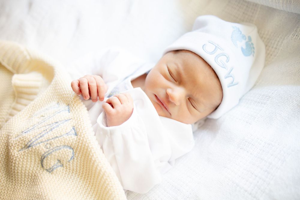 Sleeping newborn baby in white outfit and monogrammed hat, wrapped in a soft yellow knit blanket University of Tennessee Medical Center.