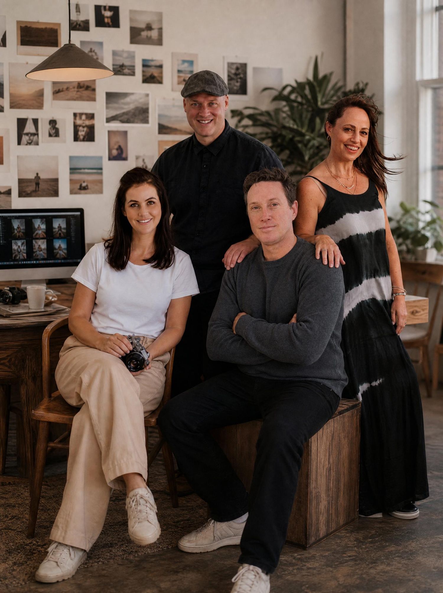 A smiling couple poses in a modern white kitchen, woman holding a camera, man in a cap leaning on the counter.