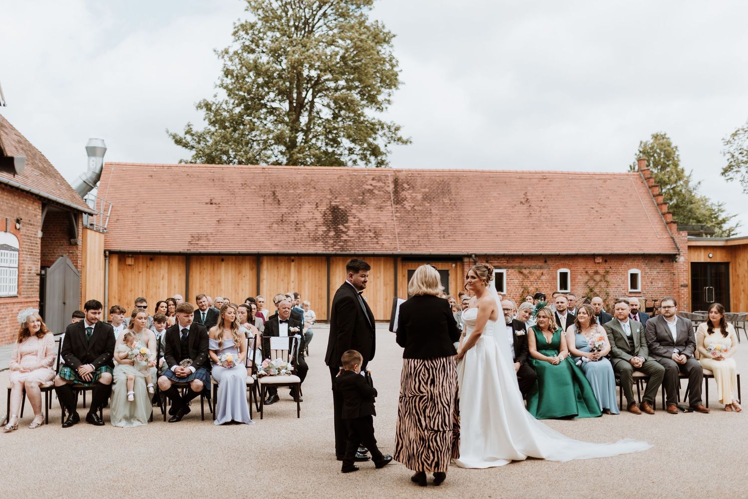 Outdoor wedding ceremony at a rustic barn venue with guests seated, bride and groom at the altar.