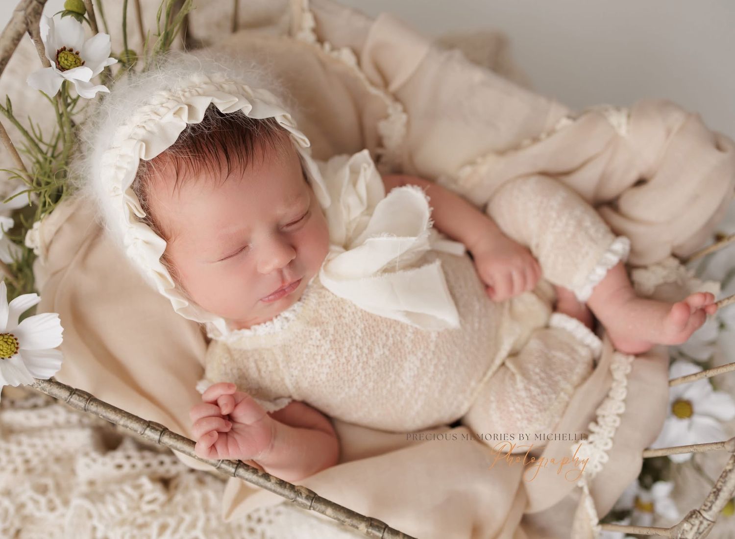 Sleeping newborn baby girl in pink lace romper and bow headband on soft pink blanket.