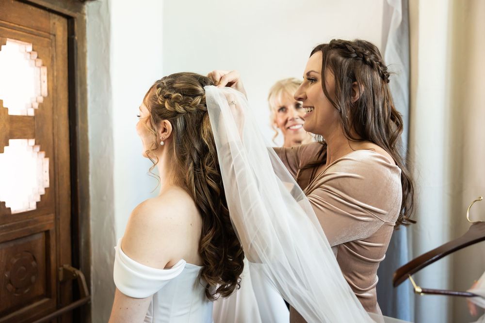 Bridesmaids helping a bride with her veil and hair before the wedding ceremony indoors.