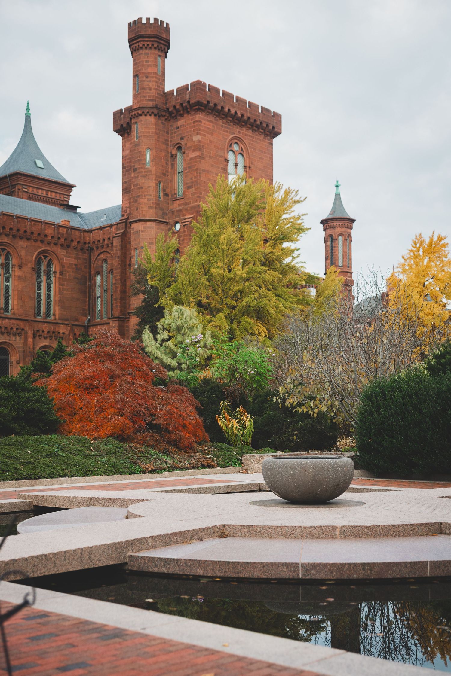 Smithsonian Castle red brick Gothic building with autumn trees and reflecting pool in foreground, Washington DC.
