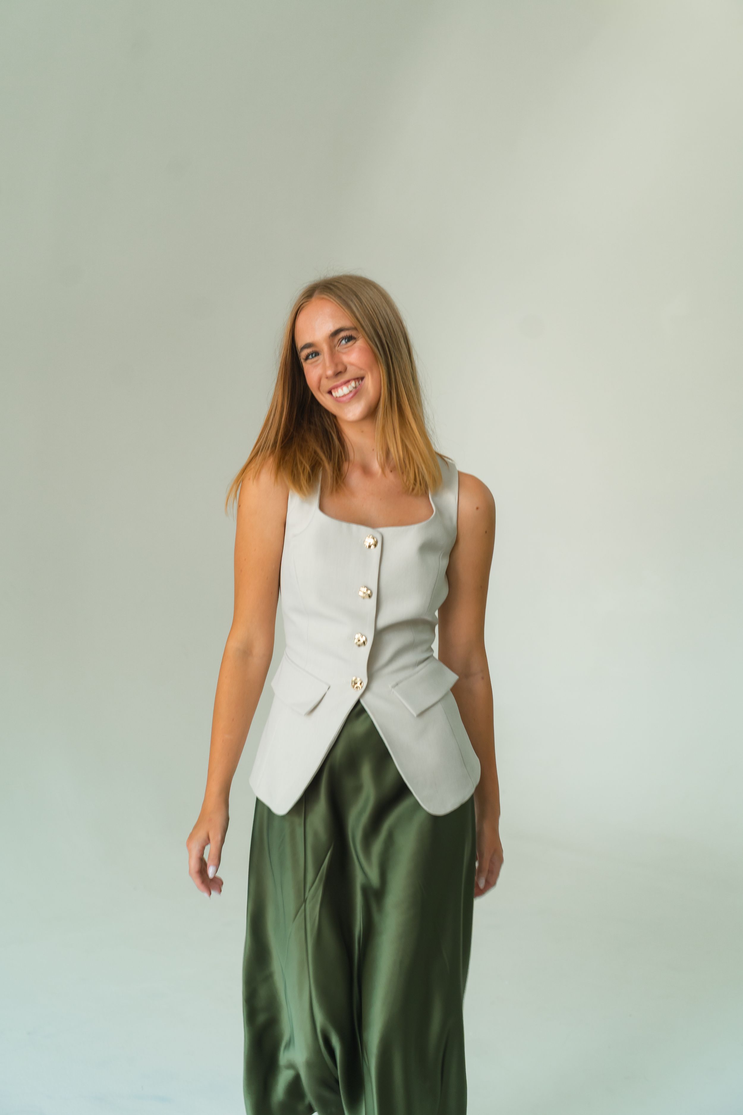 Smiling woman wearing a white linen vest top and olive green wide-leg satin trousers against a light background.