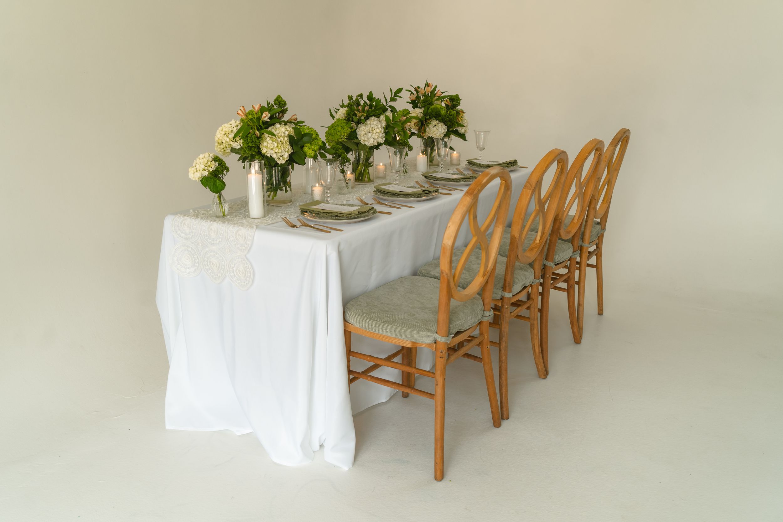 Elegant wedding reception table with white linen, gold chairs, and lush floral centerpieces in a neutral studio setting.