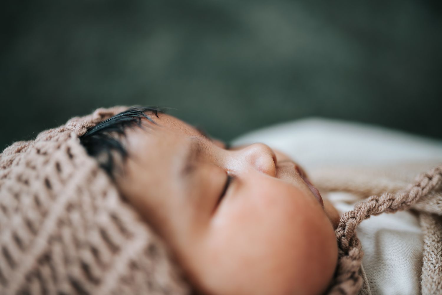 Peaceful newborn baby sleeping wrapped in a cozy knit blanket with dark hair visible.