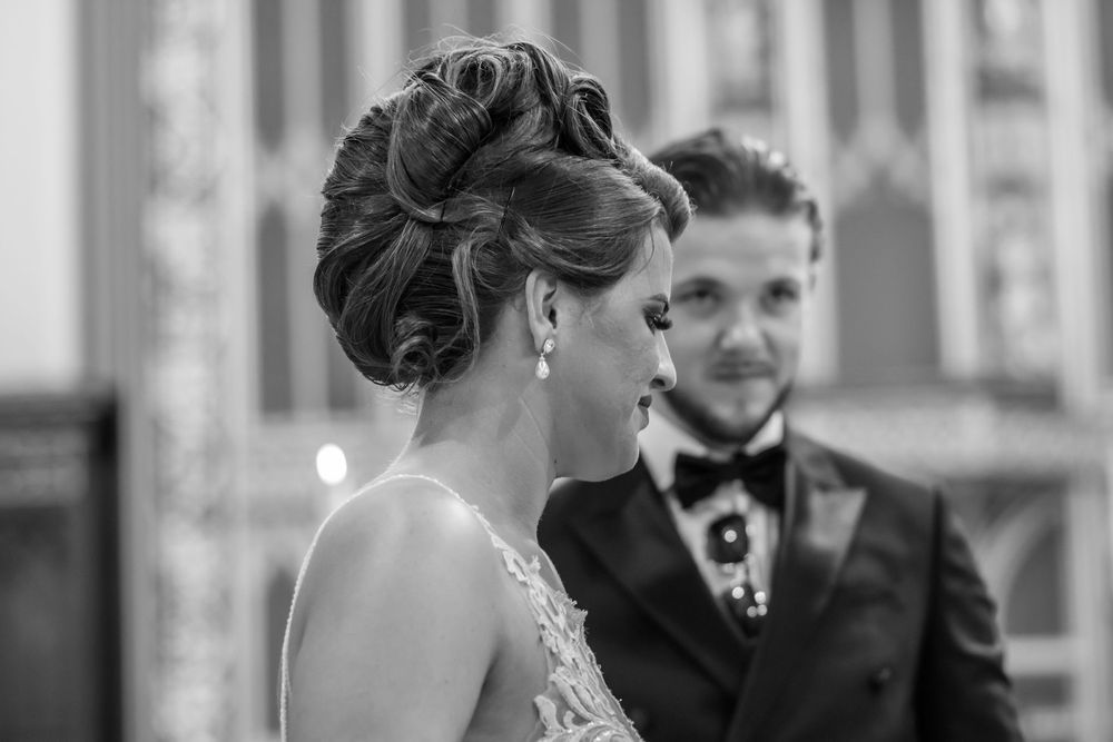 Black and white wedding photo of bride with elegant updo hairstyle and groom in bow tie standing together.