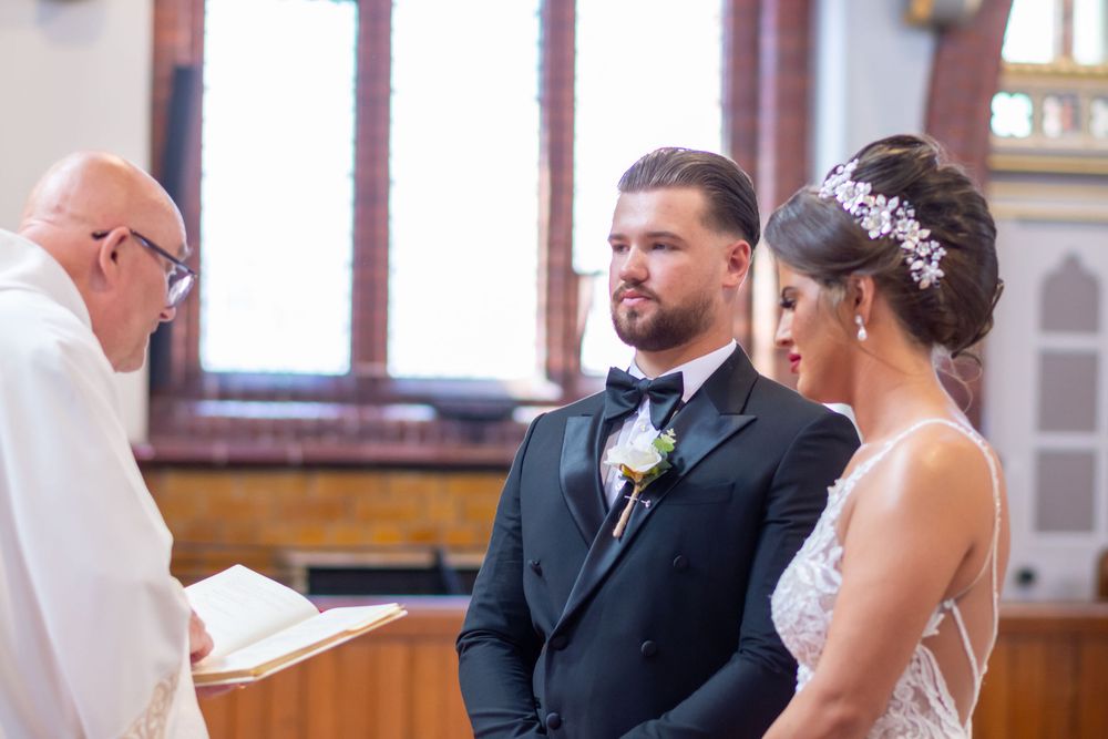 Bride and groom stand at the altar during a church wedding ceremony as an officiant reads from a book.