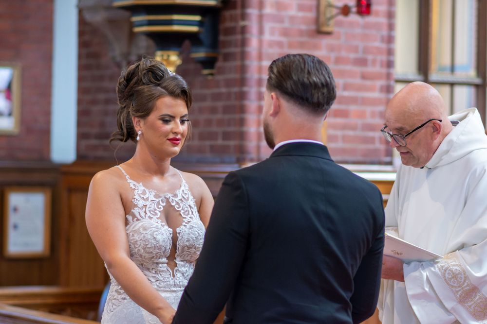 Bride and groom exchange vows before priest during intimate church wedding ceremony.