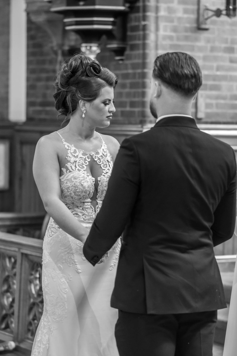 Black and white photo of a bride and groom holding hands at the altar during their wedding ceremony.