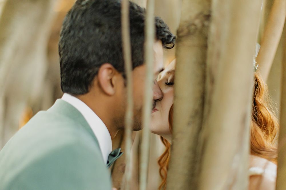 A bride and groom share a romantic kiss framed by golden bamboo stalks during their outdoor wedding ceremony.