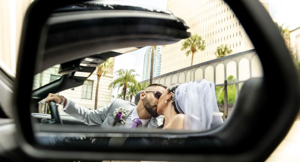 Couple sharing a kiss reflected in a car side mirror on their wedding day with palm trees in background.