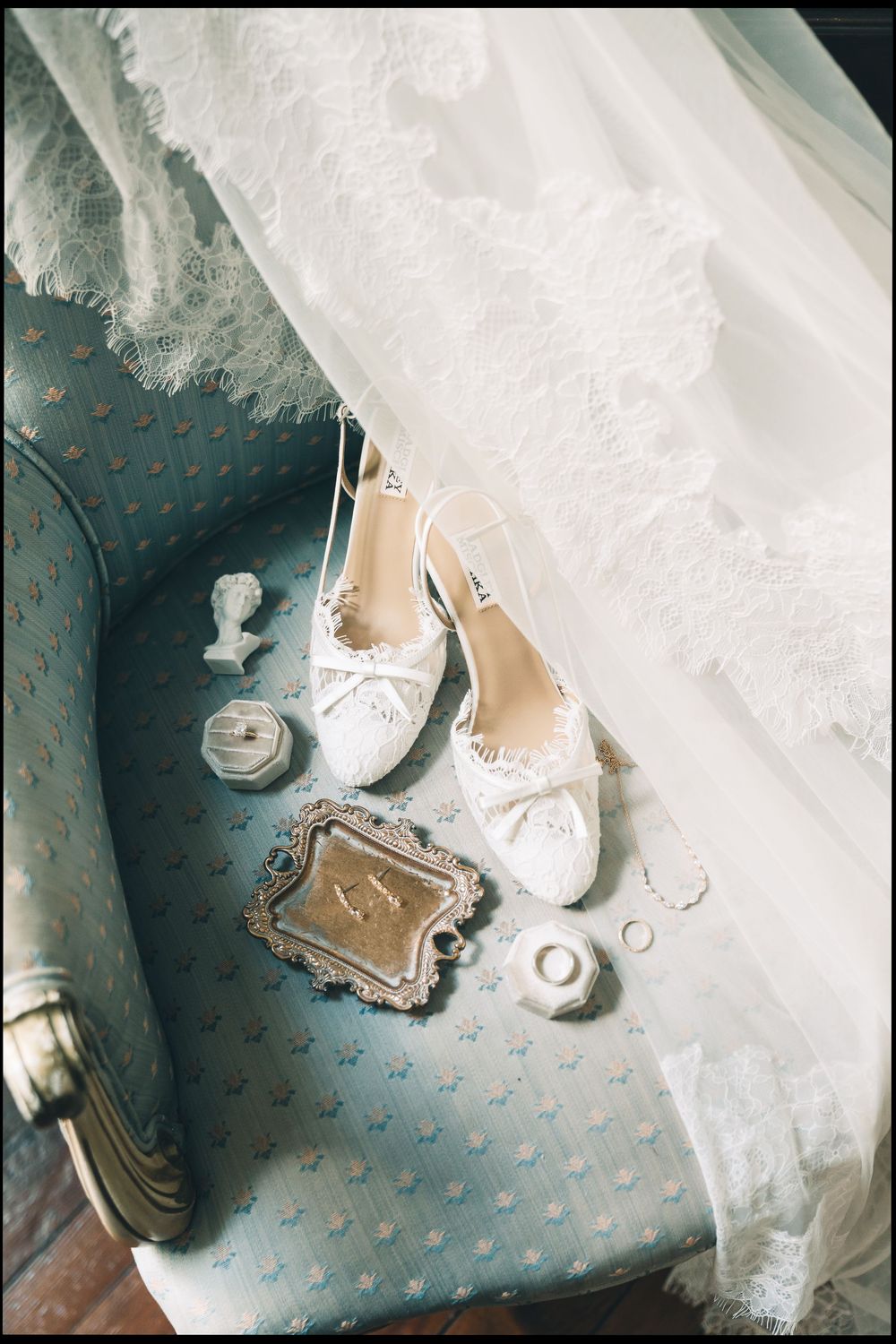 White lace bridal shoes on vintage blue chair with wedding rings, veil, and elegant accessories for a romantic wedding day.